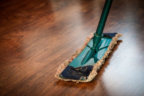 This is a picture of a green dust mop on a clean and shiny dark brown hardwood floor.