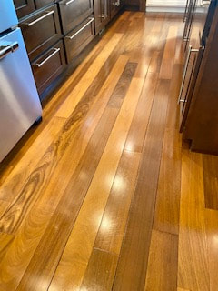 A picture of a lustrous, polished hardwood floor in a kitchen. It is so shiny you can see the reflection of the light fixtures overhead.