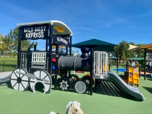 A picture of a children's playground and slide built in the shape of an old-time steam locomotive engine at the Wild West Jordan playground located within the West Jordan Veteran's Memorial Park.
